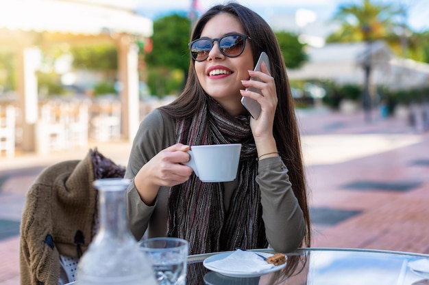 Kobieta rozmawiająca przez telefon podczas picia kawy w kawiarni na świeżym powietrzu