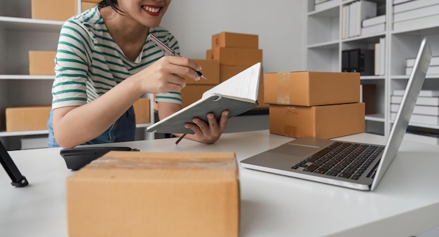 Kobieta rozpoczynająca działalność jako właścicielka małej firmy, sprawdza zamówienia online, aby przygotować się do pakowania pudeł z towarami do sprzedaży klientom