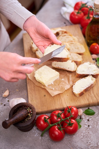 Kobieta rozprowadza smaczne organiczne masło na chlebie na szarym stole z drewnianą deską do krojenia