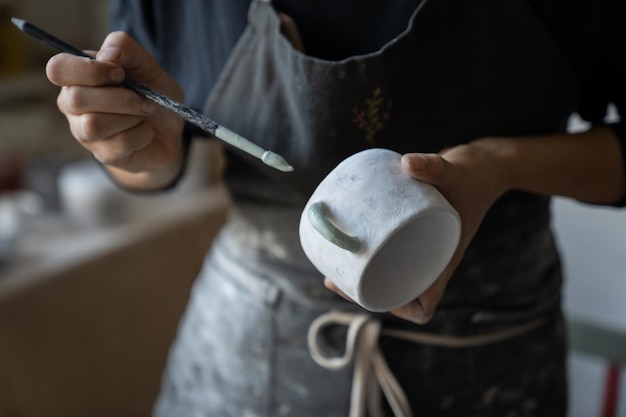Kobieta Rzemieślnik Maluje Biały Ceramiczny Kubek Z Pędzlem Stojącym W Studio Na Rozmytym Tle