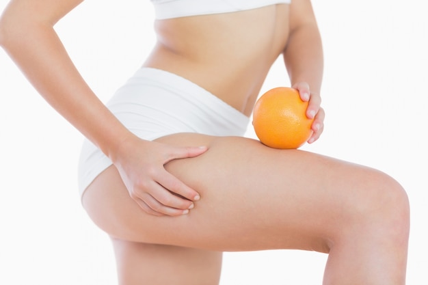 Kobieta ściska skórę na udzie, gdy trzyma pomarańczę