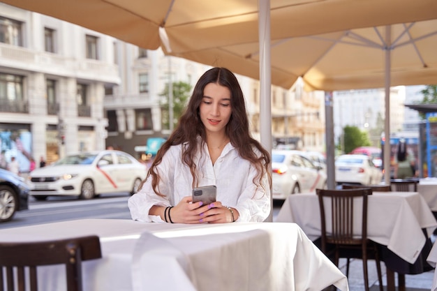 Kobieta siedząca i czekająca przy stole w kawiarni na świeżym powietrzu Kobieta patrząca na smartfona