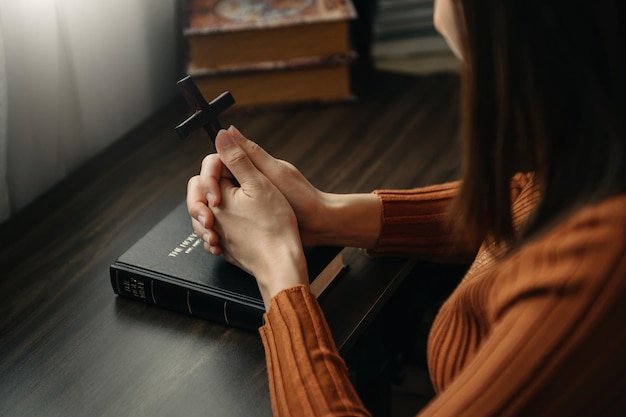 Kobieta siedząca i studiująca pisma święteDrewniany krzyż w rękach Chrześcijańskie koncepcje edukacyjne Pismo Święte otwiera się i modli się do Boga