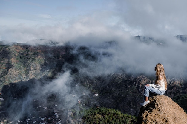Kobieta siedząca na skale z niesamowitym widokiem na Roque Nublo na Gran Canarii