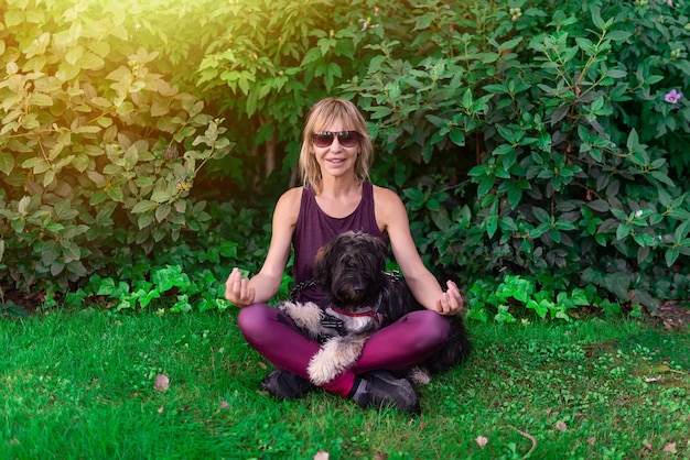 Kobieta siedząca na trawniku ze swoim owczarkiem katalońskim wykonująca ćwiczenia medytacji i jogi