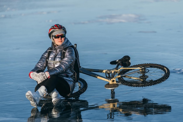 Kobieta siedząca obok roweru na lodzie Dziewczyna rowerzystka zatrzymała się na odpoczynek Siada na kole i cieszy się pięknym widokiem zachodu słońca Podróżniczka jedzie na rowerze Kobieta jedzie na rowerze po lodzie