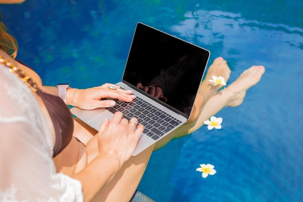 Kobieta siedząca przy basenie i korzystająca z laptopa