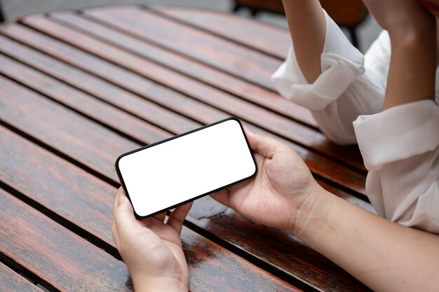 Kobieta siedząca przy stole trzymająca w pozycji poziomej makietę smartfona z białym ekranem