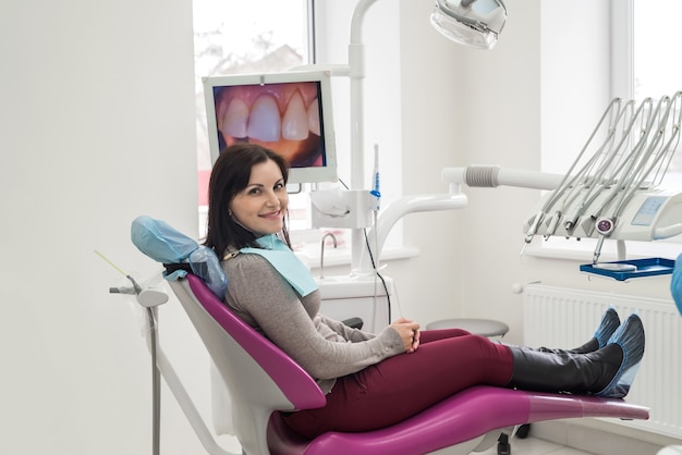 Kobieta siedzi na fotelu dentystycznym i uśmiecha się