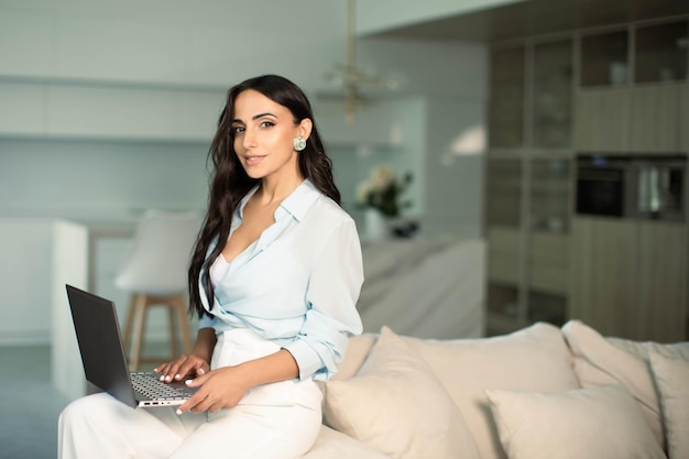 Kobieta siedzi na kanapie w mieszkaniu w domu przy użyciu laptopa