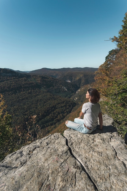 Kobieta siedzi na klifie i patrzy na dolinę w górach.