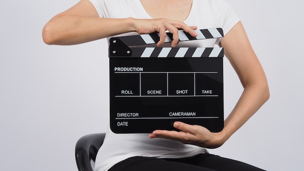 Kobieta siedzi na krześle, a ręce trzyma czarną klapę lub klapkę filmową. wykorzystuje się go w produkcji wideo, filmie, przemyśle kinowym na białym tle.