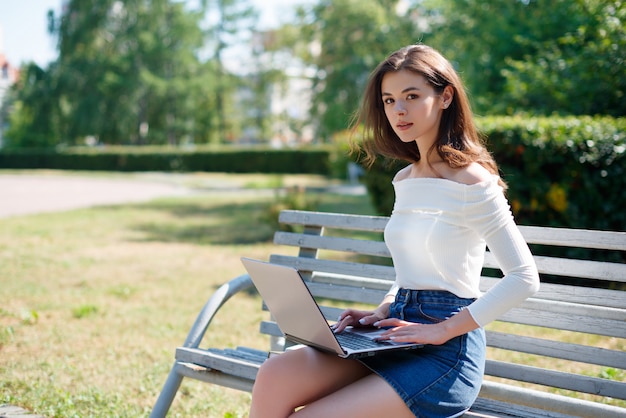 Kobieta siedzi na ławce w parku i pracuje na laptopie