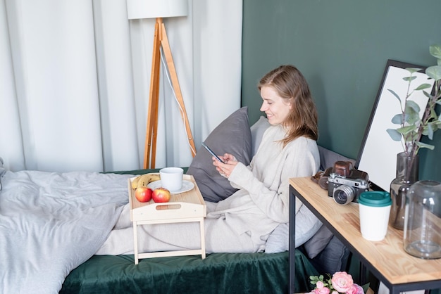 Kobieta siedzi na łóżku w domu pijąc kawę