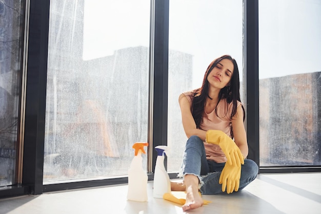 Kobieta siedzi na parapecie z butelkami sprayu do czyszczenia i rękawiczkami