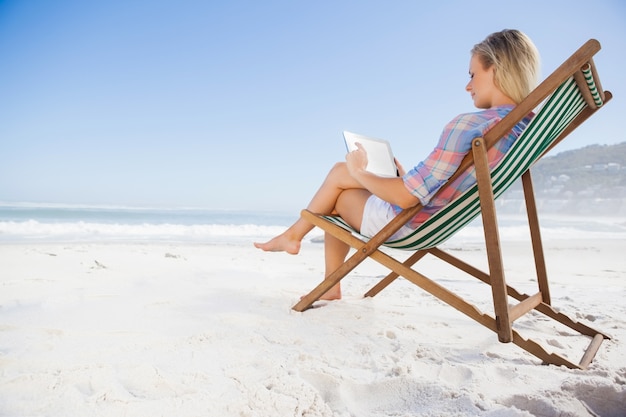 Kobieta siedzi na plaży w leżaku przy użyciu komputera typu tablet