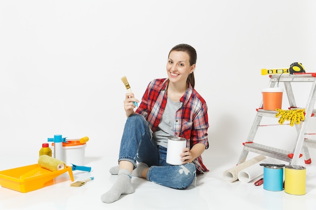 Kobieta siedzi na podłodze z pędzlem, puszkami z farbą, narzędziami do remontu pokoju na białym tle. Tapeta, akcesoria do klejenia, narzędzia malarskie. Naprawa koncepcji domu. Skopiuj miejsce