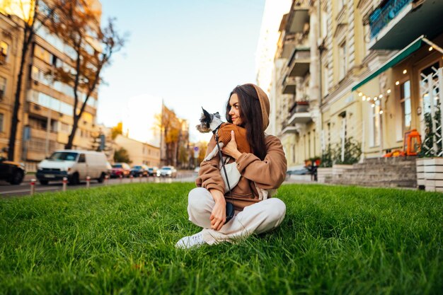 kobieta siedzi na zielonym trawniku na miejskiej ulicy ze swoim uroczym małym terierem yorkie