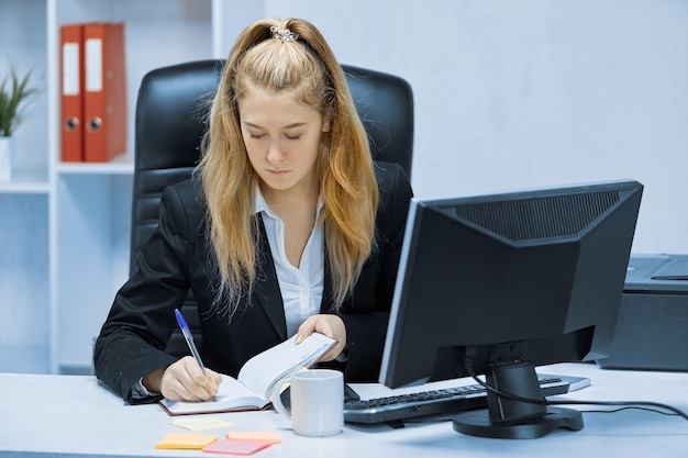 Zdjęcie kobieta siedzi przy biurku w biurze i pisze w zeszycie