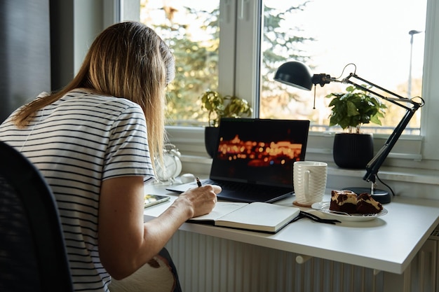 Kobieta siedzi przy stole przy oknie i korzysta z laptopa