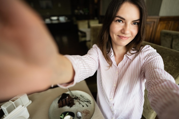 kobieta siedzi w kawiarni kawiarni restauracji w pomieszczeniu trzymać aparat i robić selfie