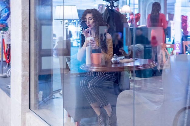 kobieta siedzi za szklanką w kawiarni i pije kawę ze słomki