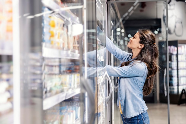 Kobieta sięgająca po mleko w lodówce w supermarkecie