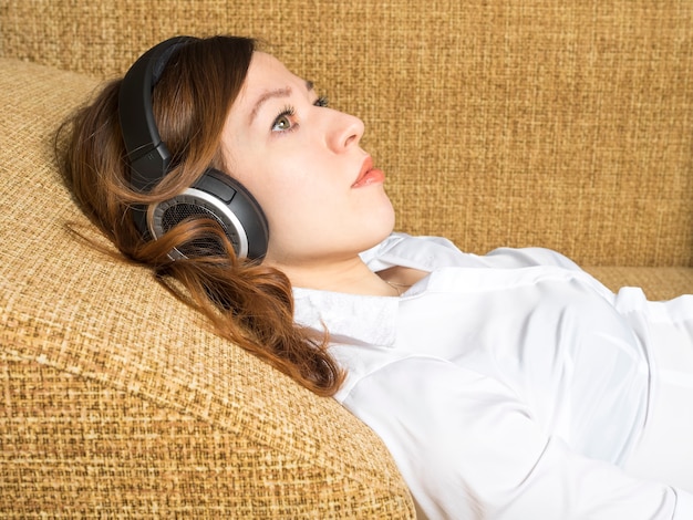 Kobieta słuchania muzyki w słuchawkach, leżąc na kanapie