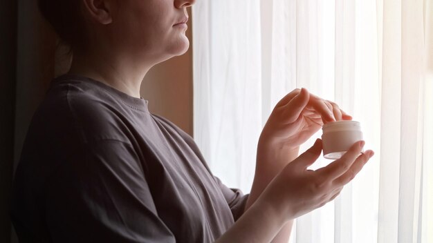 Kobieta Smaruje Ręce Kremem Nawilżającym Patrząc W Okno