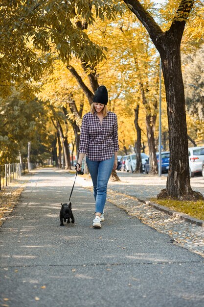 Kobieta spacerująca buldogiem francuskim w jesiennych liściach