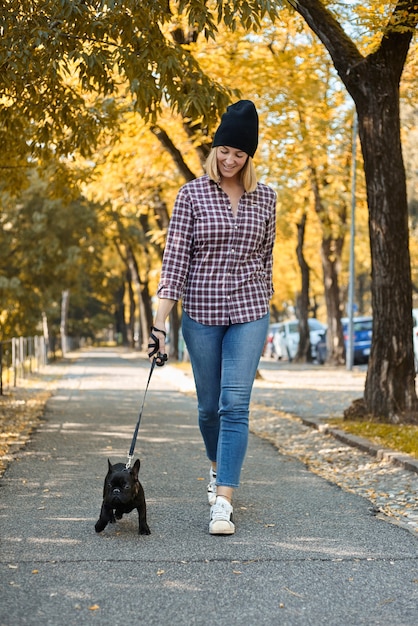 Kobieta spacerująca buldogiem francuskim w jesiennych liściach