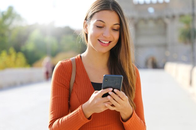 Kobieta spacerująca po mieście, wysyłająca wiadomość tekstową na telefon komórkowy