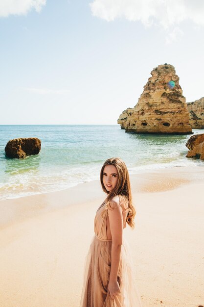 Kobieta spacerująca po plaży na tle skał i oceanu