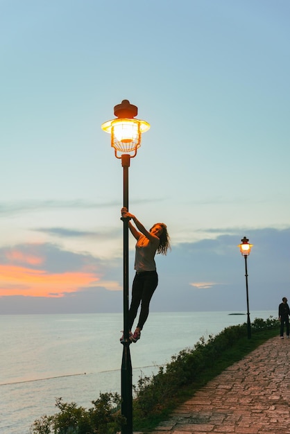 Kobieta spacerująca przez park w pobliżu morza na lampach świetlnych o zachodzie słońca