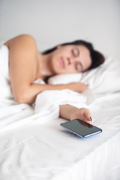 Kobieta śpiąca w łóżku z telefonem w dłoni