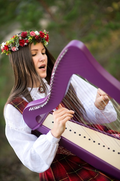 Kobieta śpiewa i gra na harfie, siedząc na zewnątrz