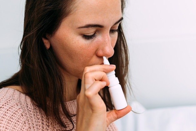 Kobieta spryskuje jej nos lekarstwem na przeziębienie.