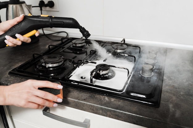 Kobieta sprzątająca paruje i dezynfekuje kuchenkę w kuchni Pracownik domowej usługi sprzątania czyści za pomocą maszyny parowej Czyszczenie parowe kuchni za pomocą profesjonalnego generatora pary