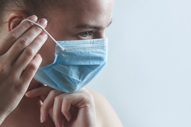 Kobieta stawia na ochronną maskę medyczną z bliska na białym tle. Ochrona przed koronawirusem, kurzem, miejskim smogiem, grypą, zanieczyszczeniem powietrza