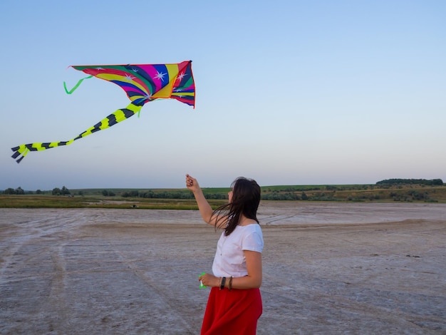 Kobieta steruje kolorowym latawcem o zachodzie słońca na plaży Koncepcja spędzania wspaniałego czasu w lecie Relaks Ptak szybuje na niebie Latający latawiec z zawieszonym w powietrzu Ogon latawca kołysze się na wietrze Wolność