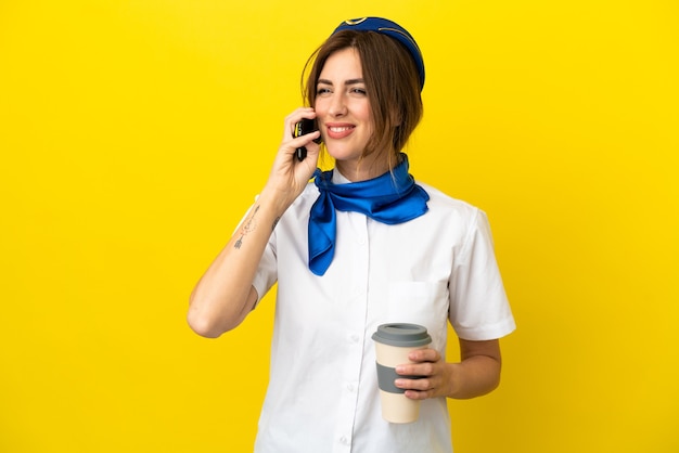 Kobieta stewardesa samolotu na białym tle na żółtym tle trzymająca kawę na wynos i telefon komórkowy