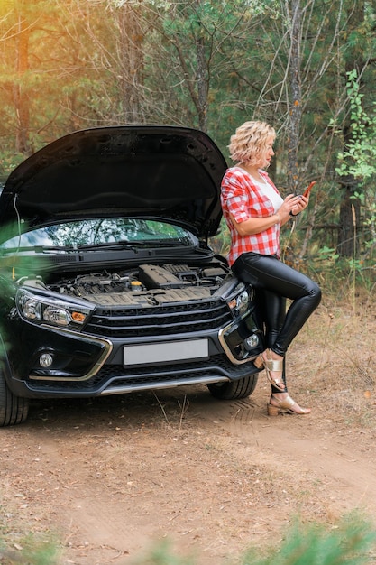 Zdjęcie kobieta stoi przy otwartej masce samochodu i dzwoni telefonicznie na pogotowie