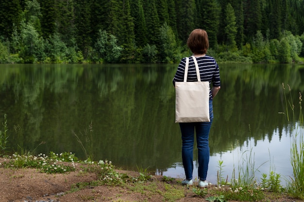 Kobieta stojąca na brzegu jeziora niosąca makietę pustą torbę na zakupy wielokrotnego użytku