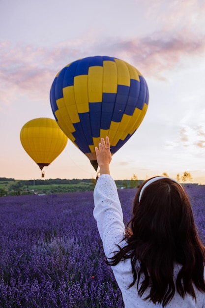 Kobieta stojąca na lawendowym polu patrząca na balony z koszem zachodu słońca