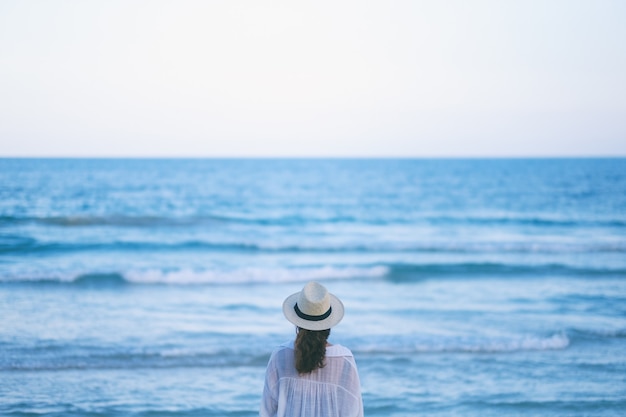 Kobieta stojąca na plaży, samotnie patrząc na piękne morze i błękitne niebo