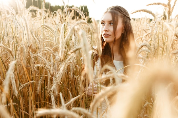 Kobieta stojąca na polu pszenicy z kłoskami i delikatnie odwracająca wzrok