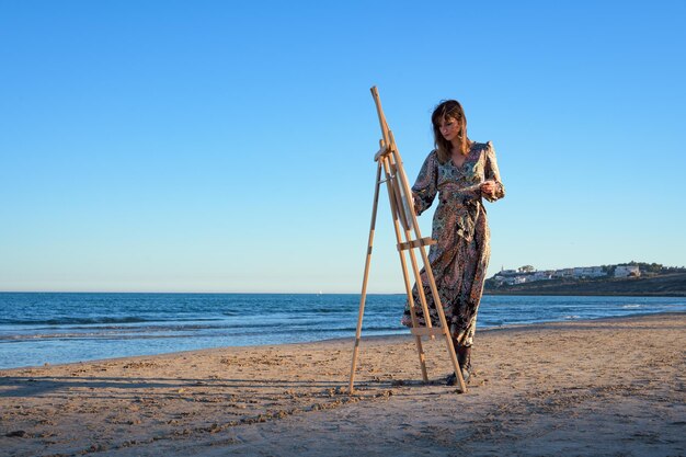 Zdjęcie kobieta stojąca obok easel na plaży