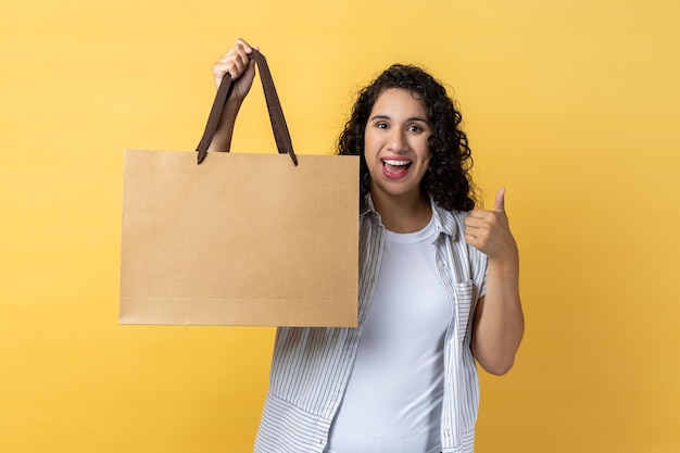 Kobieta stojąca z torbą na zakupy i pokazująca kciuk w górę poleca centrum handlowe na zakupy