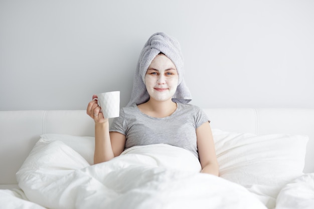 Kobieta stosująca maskę na twarz i pijąca kawę w łóżku