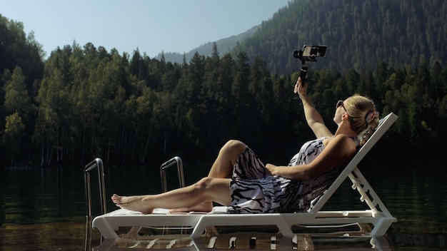 Kobieta strzelająca na ręcznym stabilizatorze gimbala na smartfonie Dziewczyna leży na leżaku na molo zrób selfie Blogger transmituje wideo vlogowanie